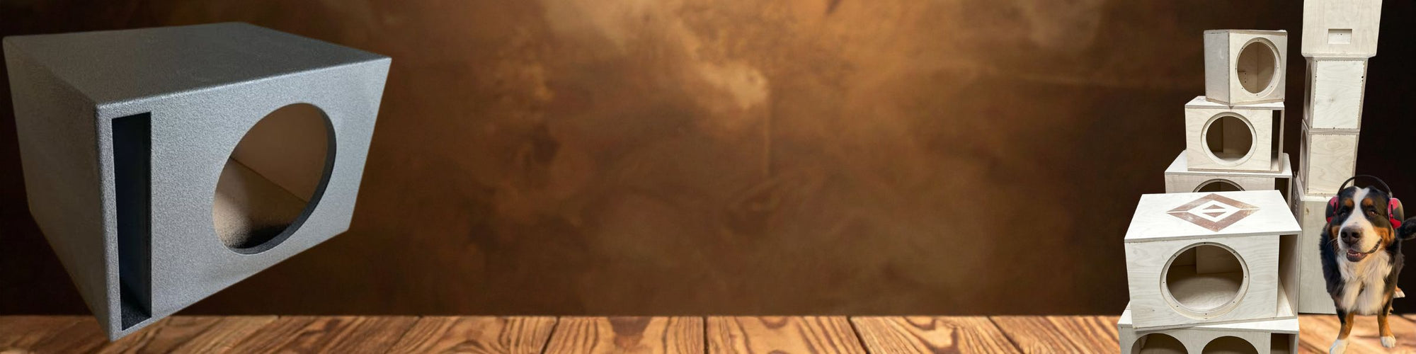 “Subwoofer enclosure boxes displayed on a wooden surface, with one gray ported box on the left and a stack of natural wood enclosures on the right.”