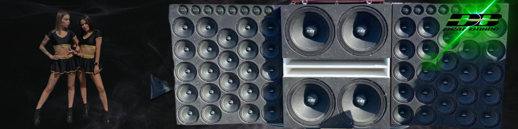 “Two women in branded black and gold outfits stand beside a large wall of car audio speakers and subwoofers, with the Deaf Bonce logo on a dark background.”